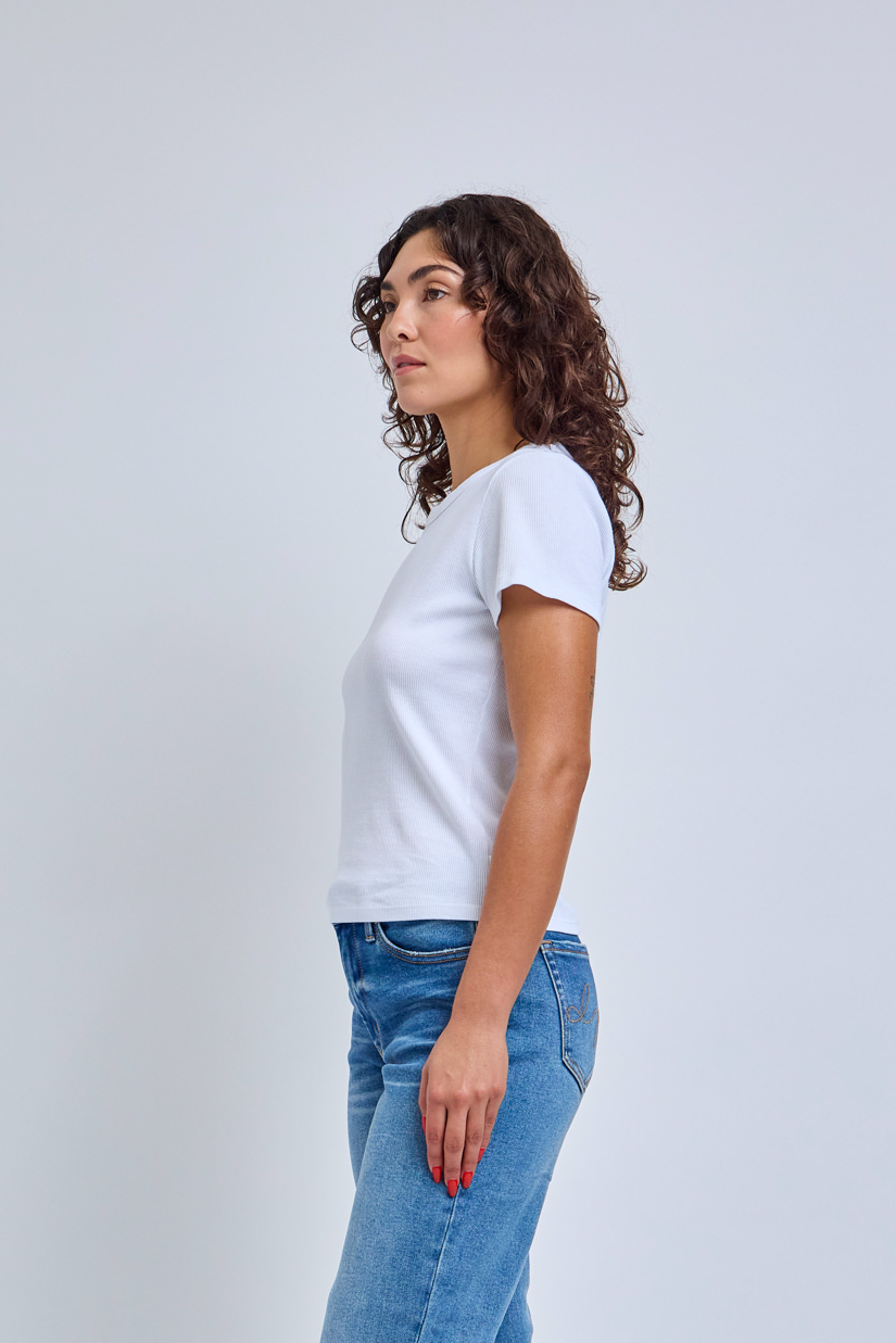 Woman wearing a white t-shirt and blue jeans against a light gray background