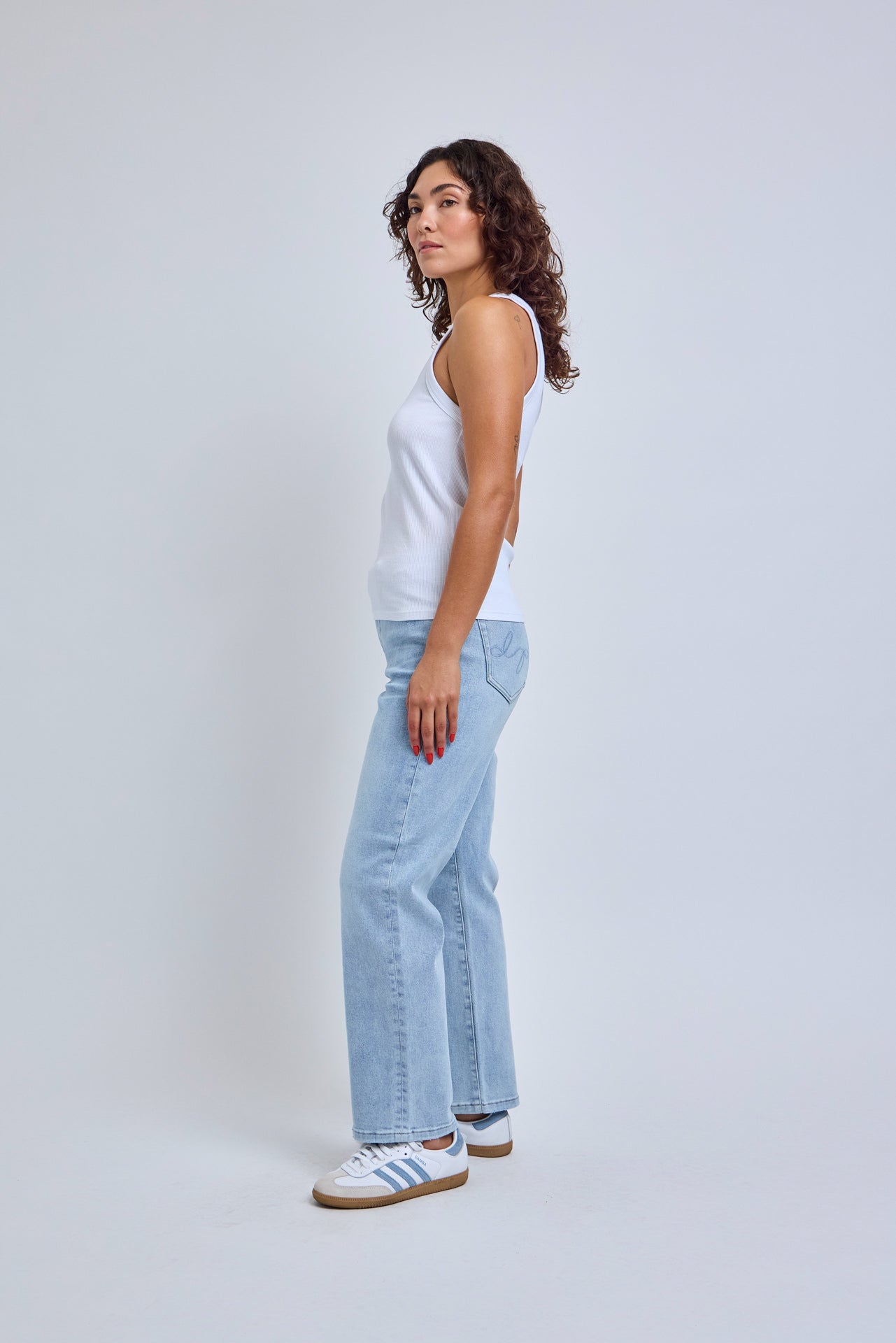 Woman wearing a white tank top and light blue jeans on a plain background
