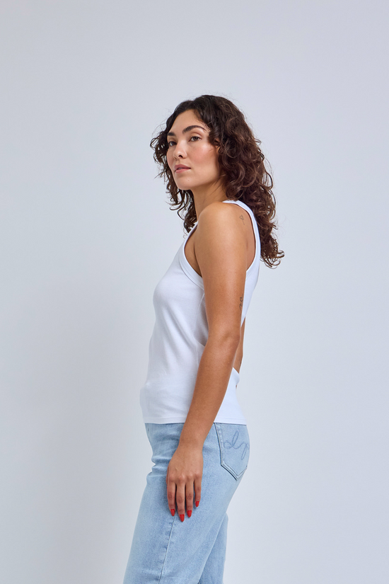 Woman wearing a white tank top and light blue jeans against a plain background
