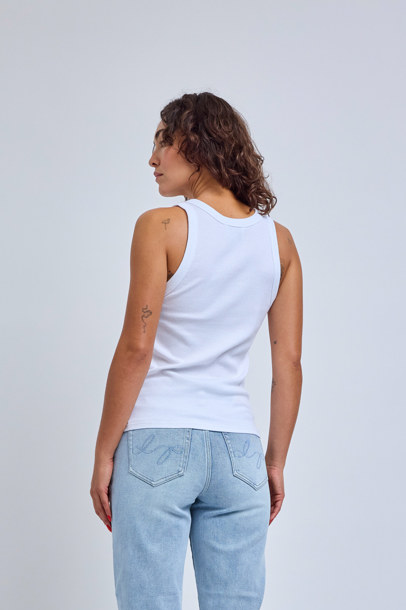 Person wearing a white tank top and light blue jeans on a plain background