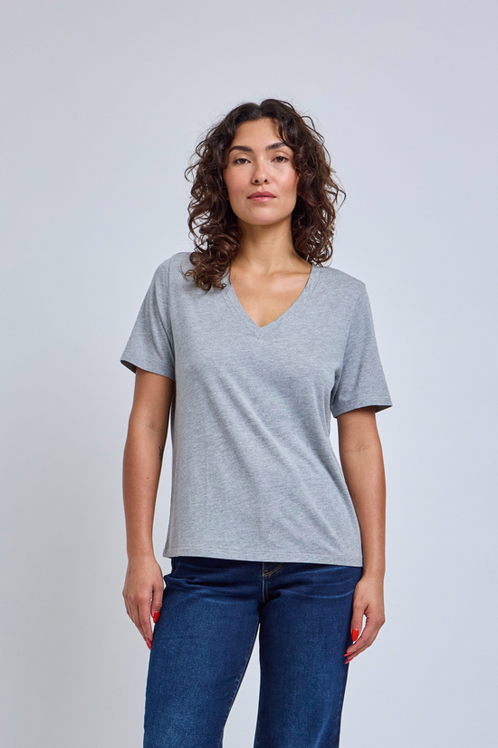 Woman wearing a gray v-neck tee and dark blue jeans against a plain background | model-size: 4