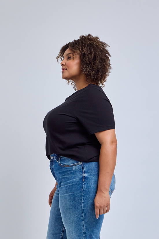 Woman wearing a black t-shirt and blue jeans against a gray background