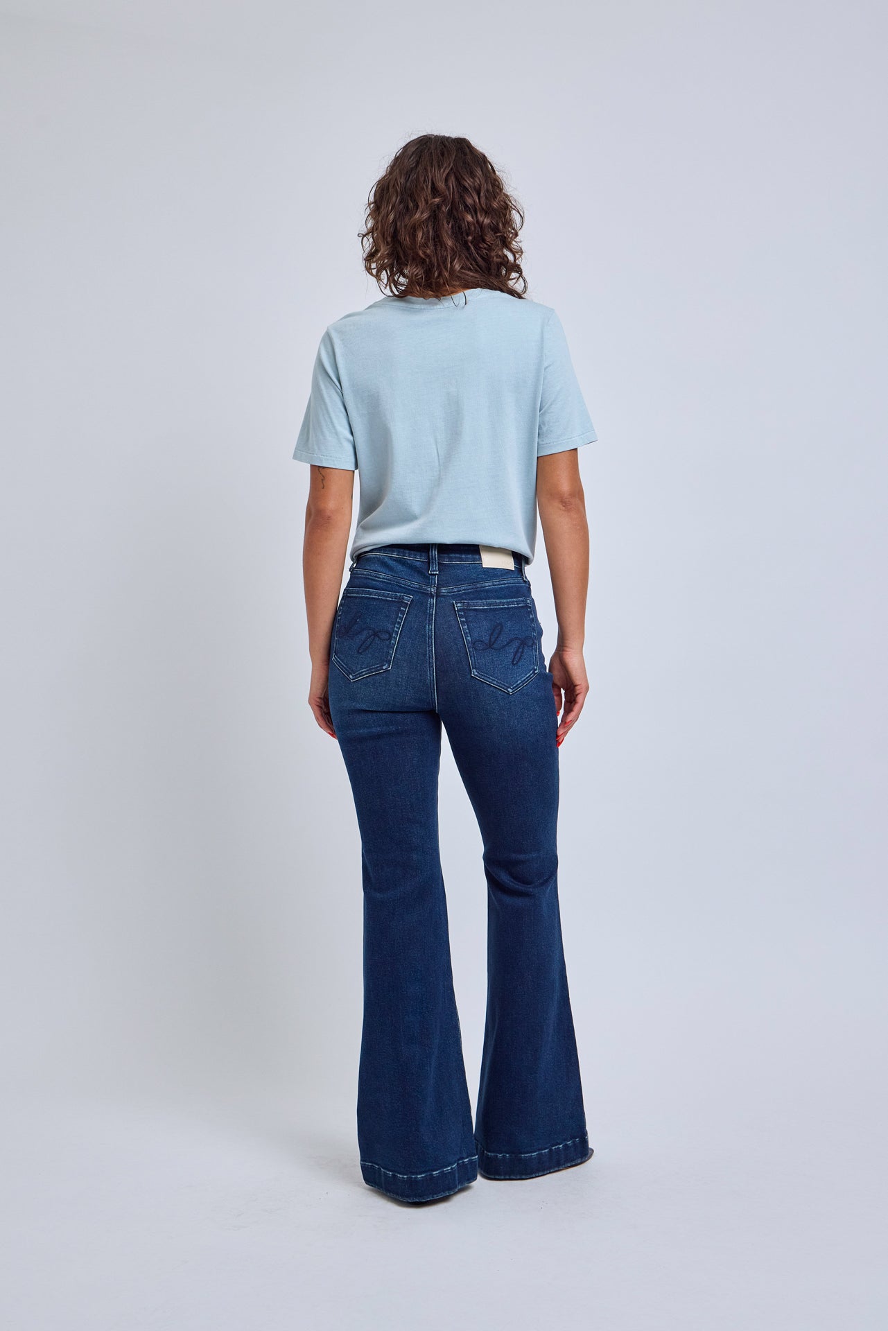Person wearing a light blue t-shirt and dark blue flared jeans on a white background
