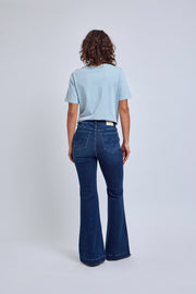 Person wearing a light blue t-shirt and dark blue flared jeans on a white background