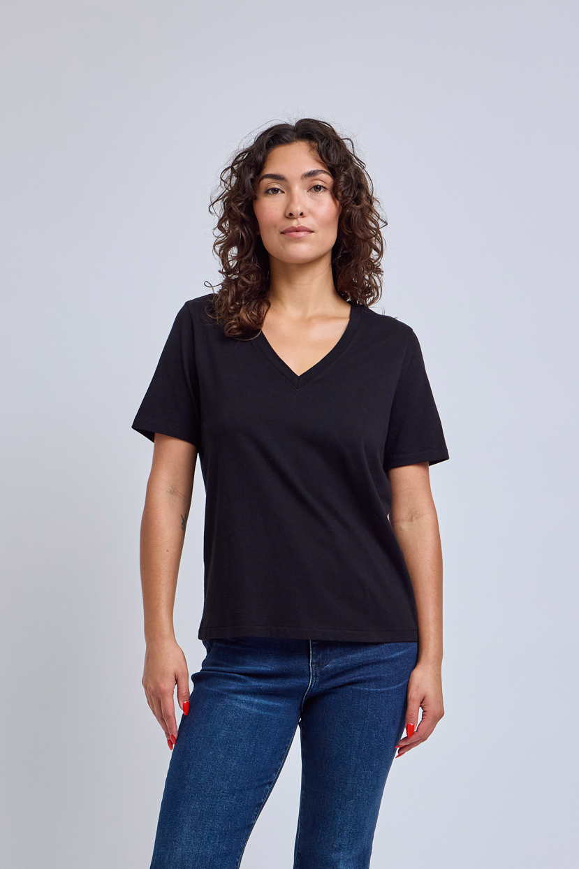 Woman wearing a black v-neck t-shirt and blue jeans against a gray wall | model-size: 4