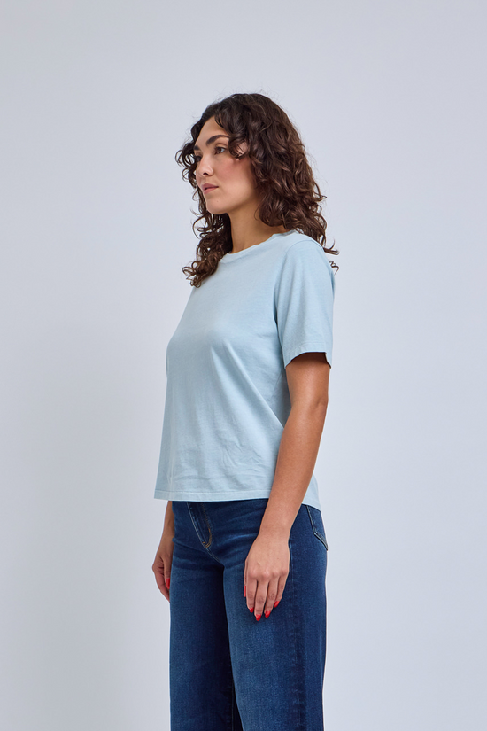 Woman wearing a light blue t-shirt and blue jeans against a white background