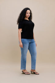 Woman wearing a black t-shirt and jeans with a beige background