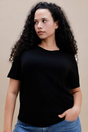 Woman wearing a black t-shirt with jeans against a beige background