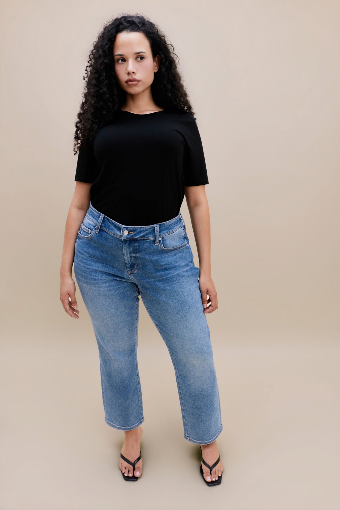 Woman wearing a black t-shirt with jeans against a beige background