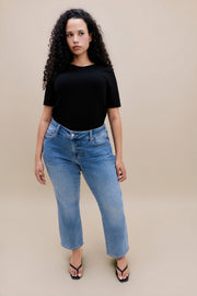 Woman wearing a black t-shirt with jeans against a beige background