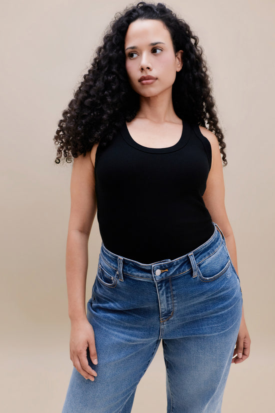 Woman wearing a black ribbed tank top and jeans against a beige background