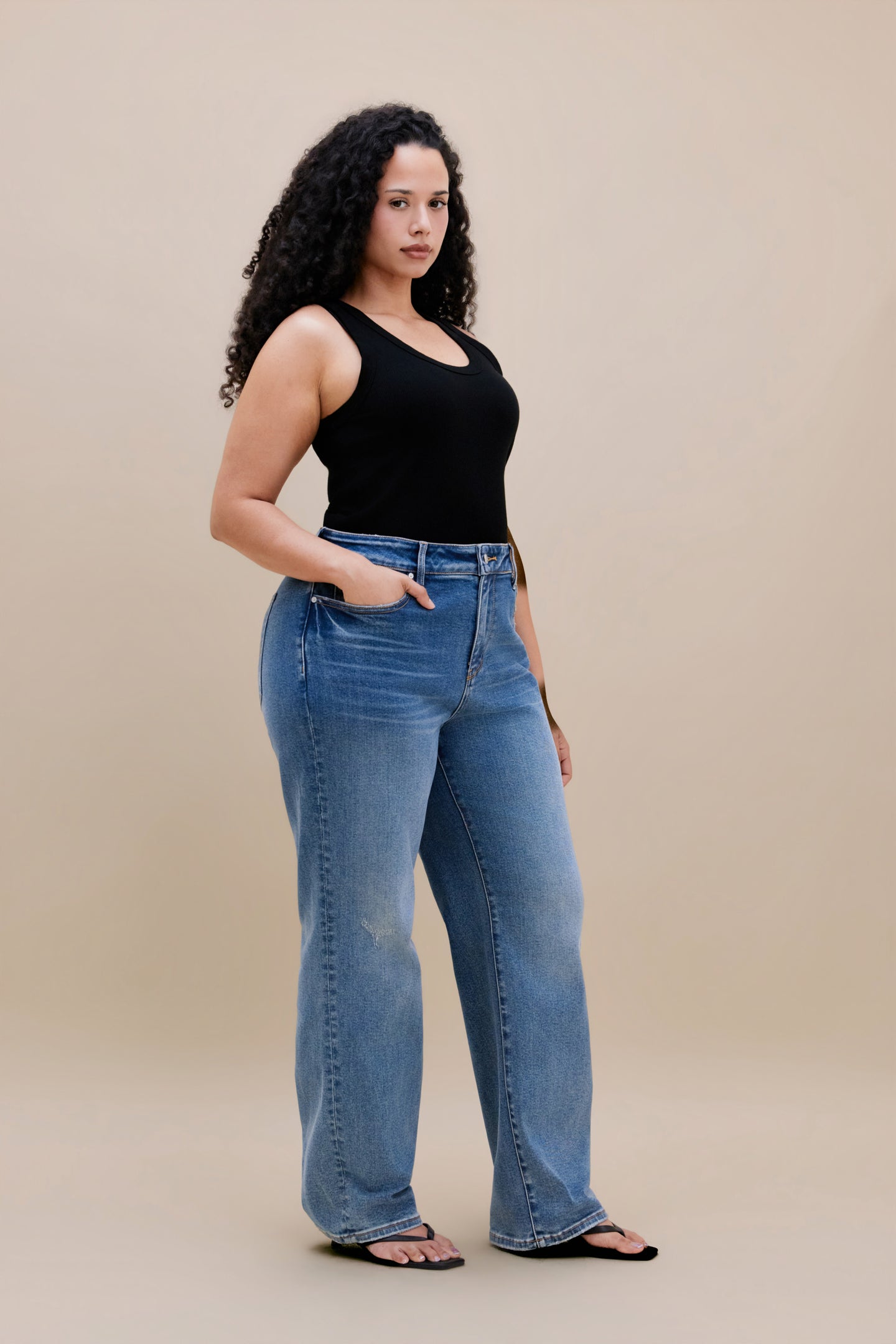 Woman wearing a black tank top and jeans with a beige background 