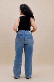 Woman wearing a black tank top and jeans with a beige background 