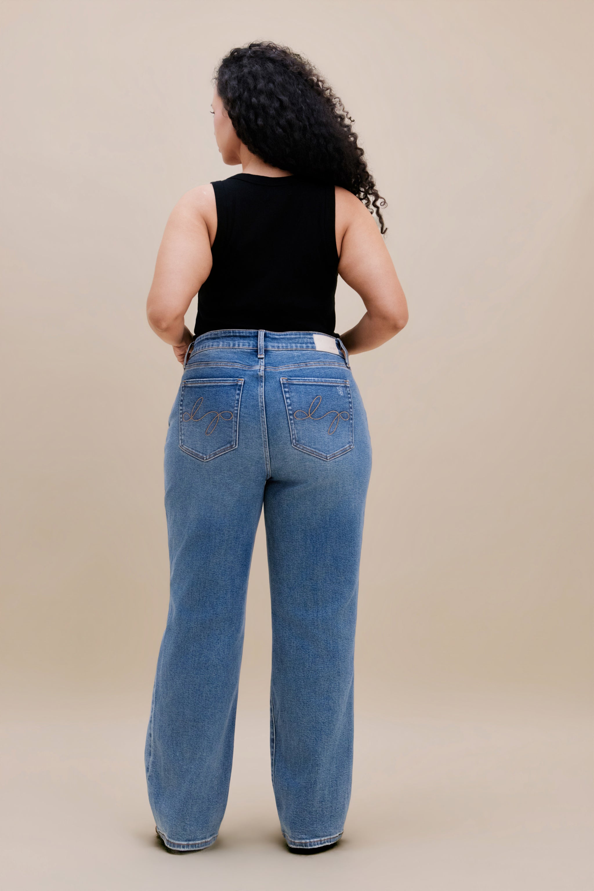Woman wearing a black tank top and jeans with a beige background 