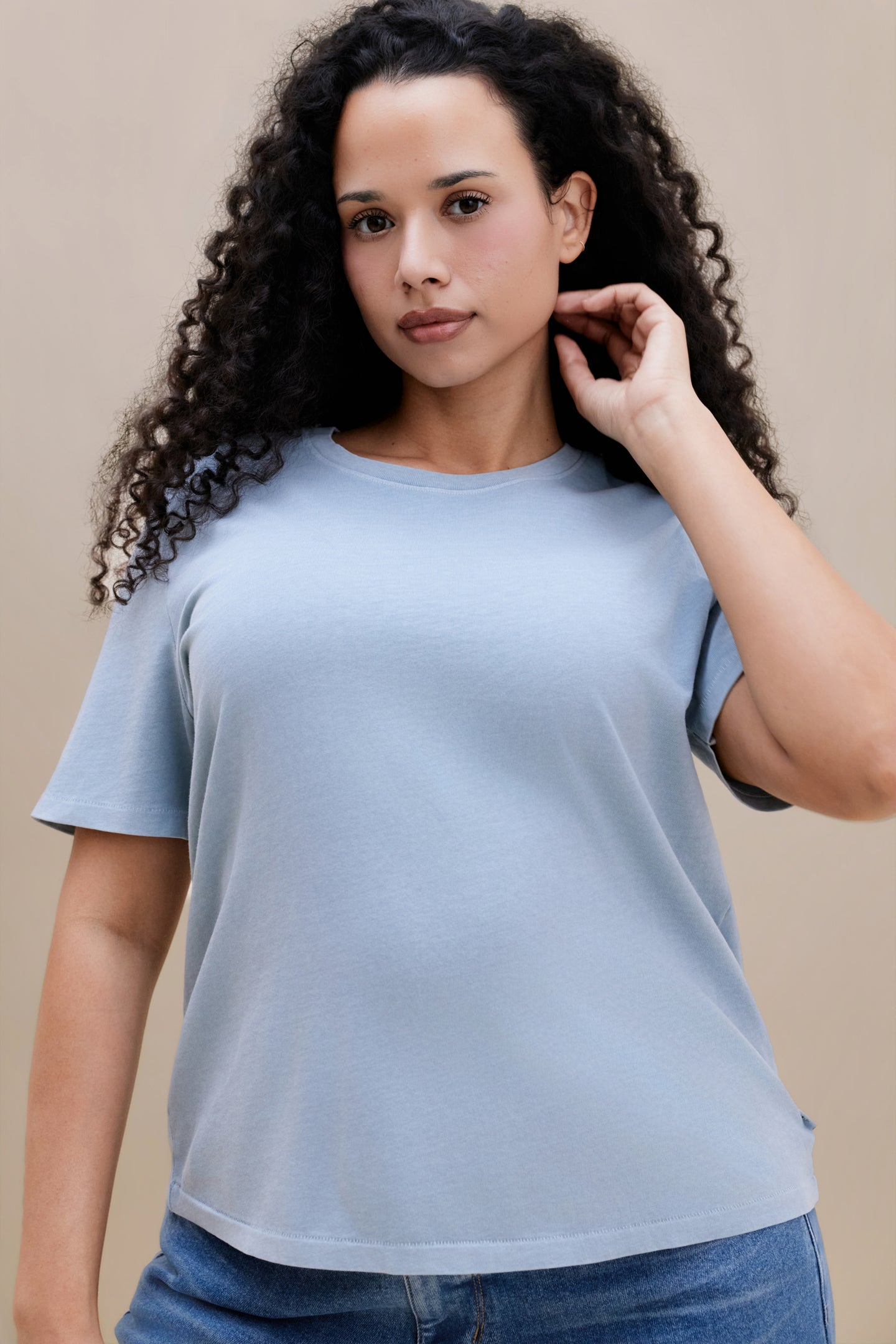 Woman wearing a blue crew neck tee and jeans with a beige background 