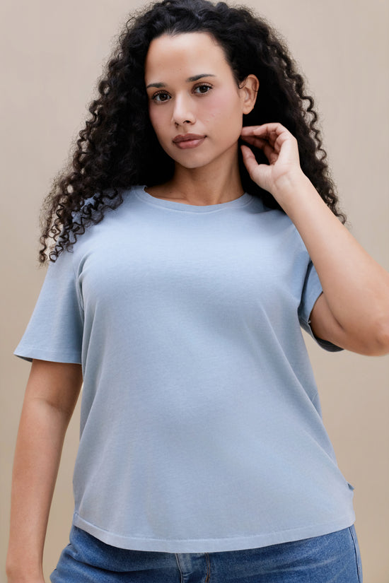 Woman wearing a blue crew neck tee and jeans with a beige background 