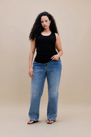 Woman wearing a black tank top and jeans with a beige background 