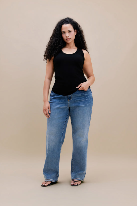 Woman wearing a black tank top and jeans with a beige background 
