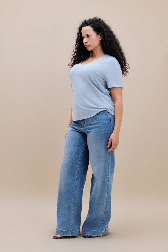 Woman wearing a blue t-shirt and wide leg jeans with a beige background