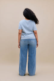 Woman wearing a blue t-shirt and wide leg jeans with a beige background