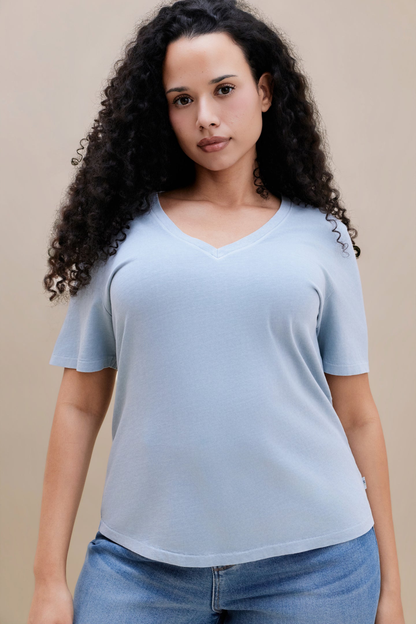 Woman wearing a blue t-shirt and jeans with a beige background