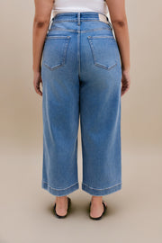 Backside bottom half of a woman wearing a white tank top with wide leg cropped jeans with a beige background 