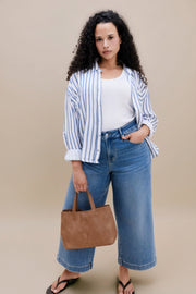 Woman wearing a white tank top and stripped blue button down shirt with wide leg cropped jeans with a beige background 