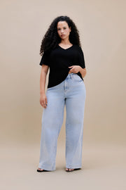 Woman wearing a black v-neck t-shirt and light colored wide leg jeans with a beige background | model-size: 16