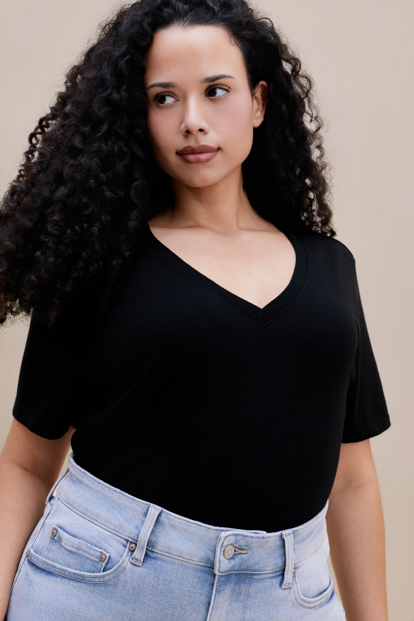 Woman wearing a black t-shirt and light blue jeans against a beige background 