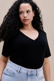 Woman wearing a black t-shirt and light blue jeans against a beige background 
