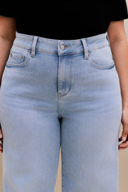 Close up highlighting the waist of a woman wearing a black v-neck t-shirt and light colored wide leg jeans with a beige background 