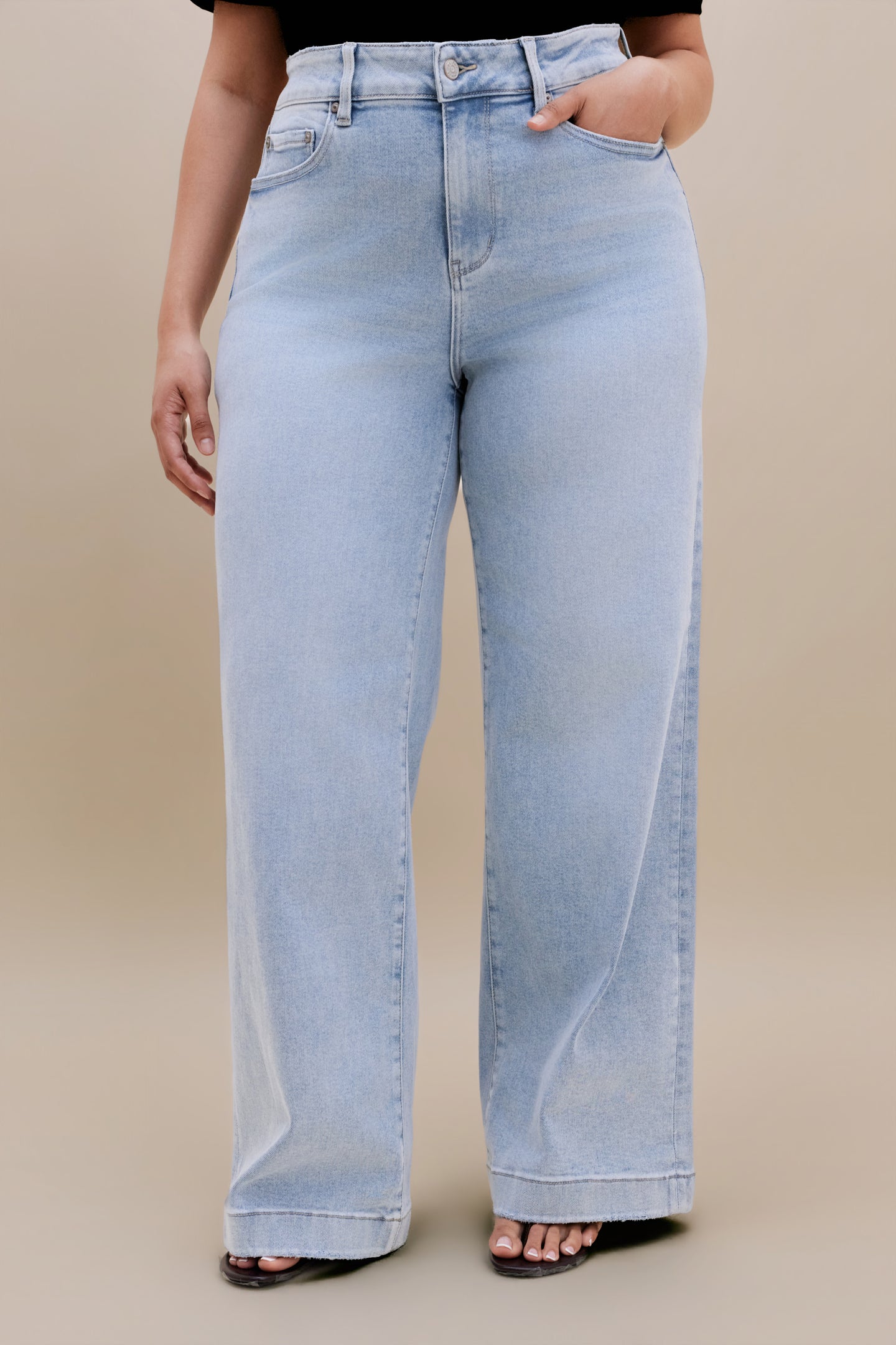 Bottom half or a woman wearing a black v-neck t-shirt and light colored wide leg jeans with a beige background 