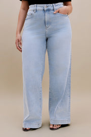 Bottom half or a woman wearing a black v-neck t-shirt and light colored wide leg jeans with a beige background 