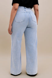 Backside bottom half of a woman wearing a black v-neck t-shirt and light colored wide leg jeans with a beige background 