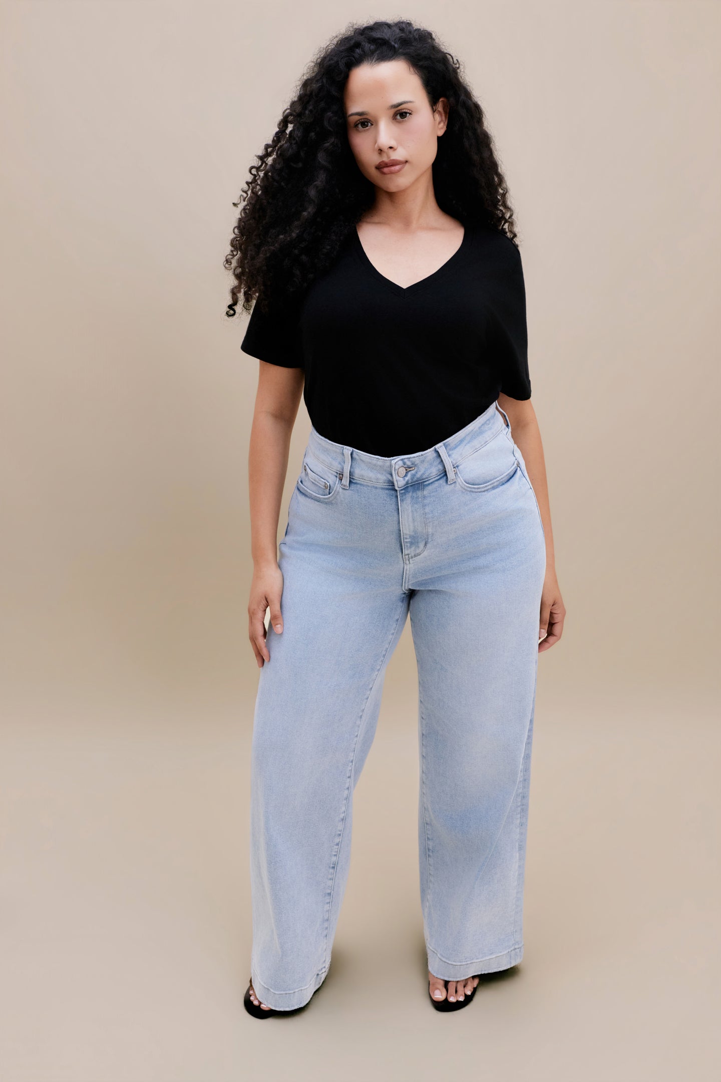 Woman wearing a black t-shirt and light blue jeans against a beige background 