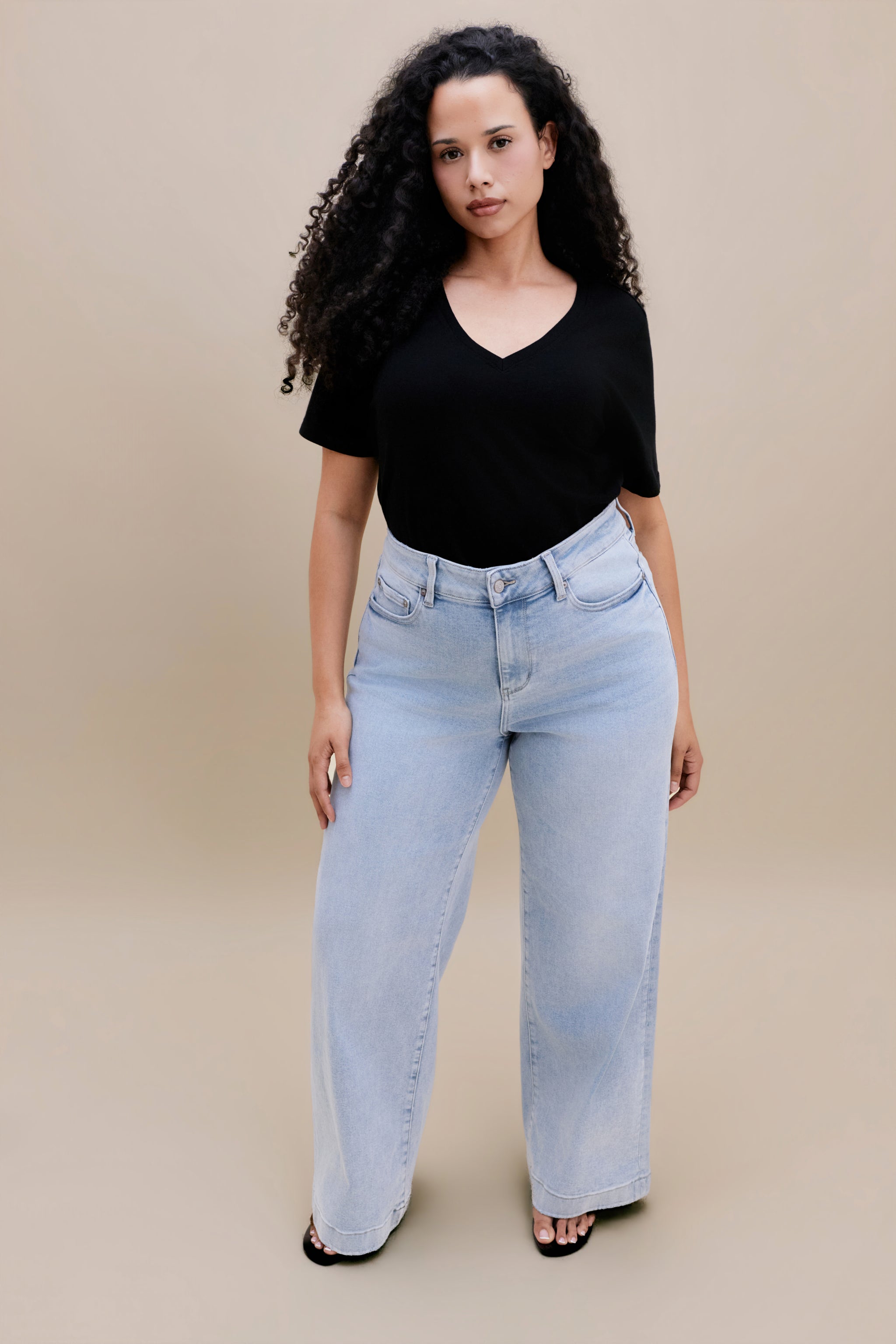 Woman wearing a black t-shirt and light blue jeans against a beige background 