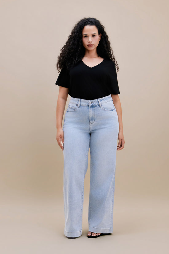 Woman wearing a black v-neck t-shirt and light colored wide leg jeans with a beige background 
