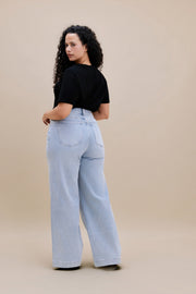 Backside of a woman wearing a black v-neck t-shirt and light colored wide leg jeans with a beige background 