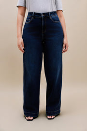 Woman wearing a gray t-shirt and dark wide leg jeans standing with a beige background