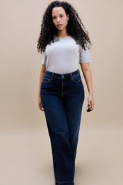 Woman wearing a gray t-shirt and dark wide leg jeans standing with a beige background