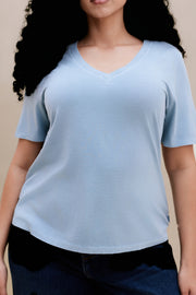 Close up a woman wearing a light blue t-shirt and dark jeans against a beige background