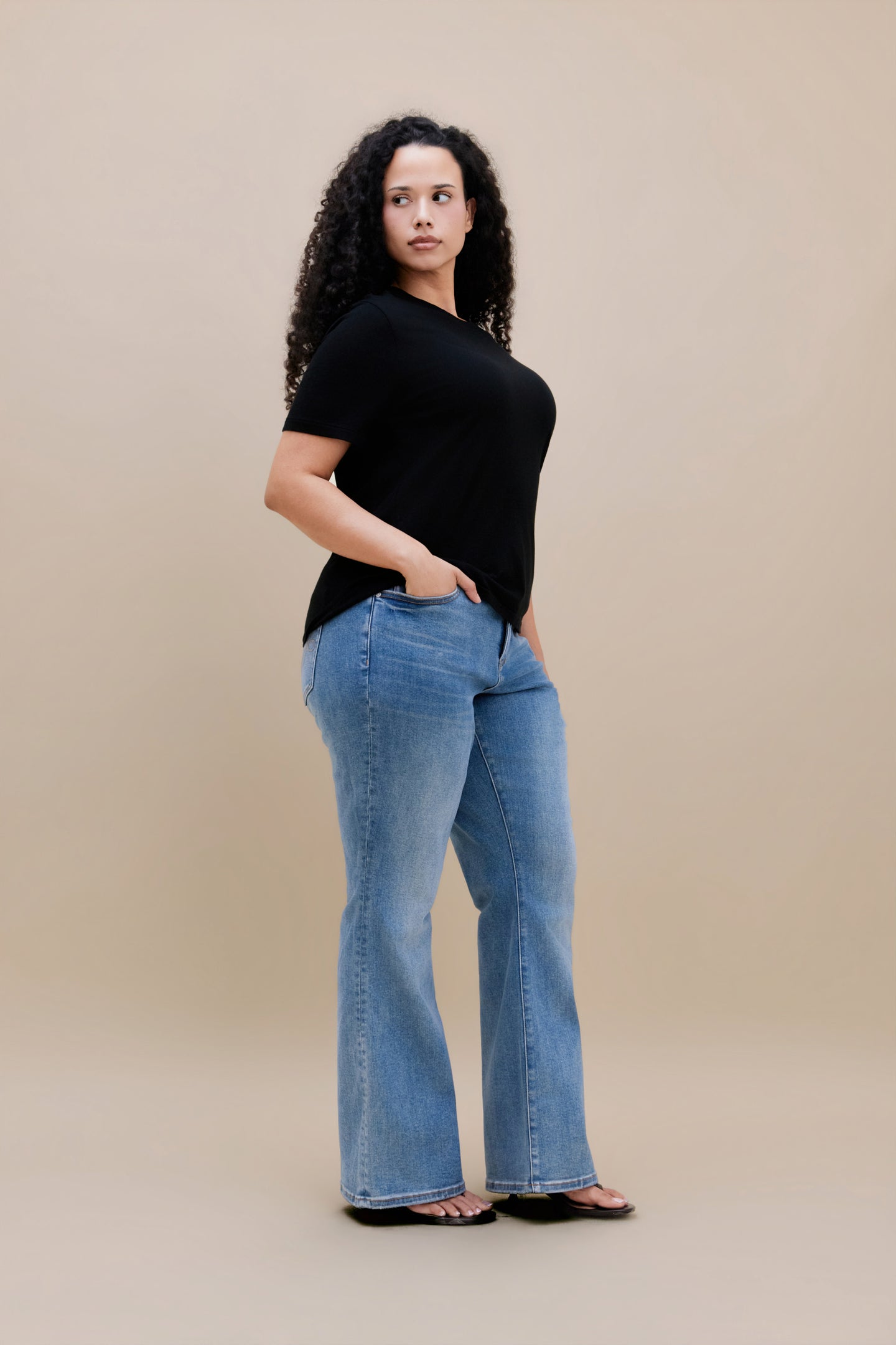 Woman wearing black t-shirt and bootcut jeans with a beige background