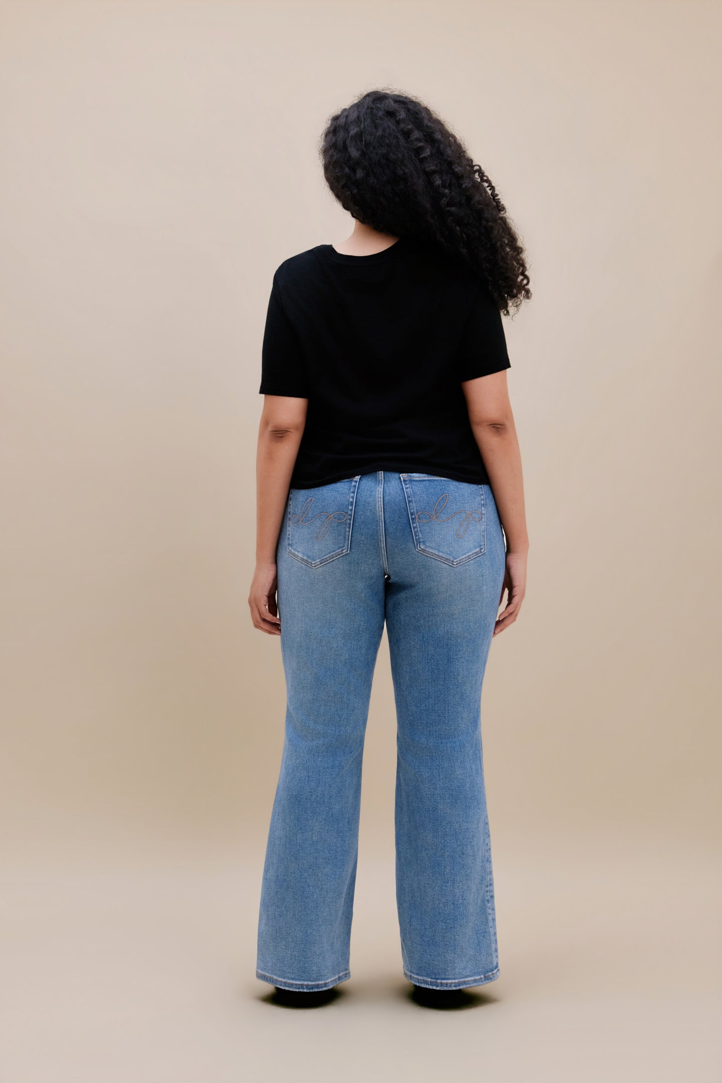 Woman wearing black t-shirt and bootcut jeans with a beige background