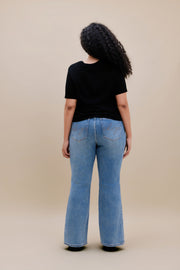 Woman wearing black t-shirt and bootcut jeans with a beige background