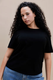 Woman wearing a black t-shirt and blue jeans against a beige background 