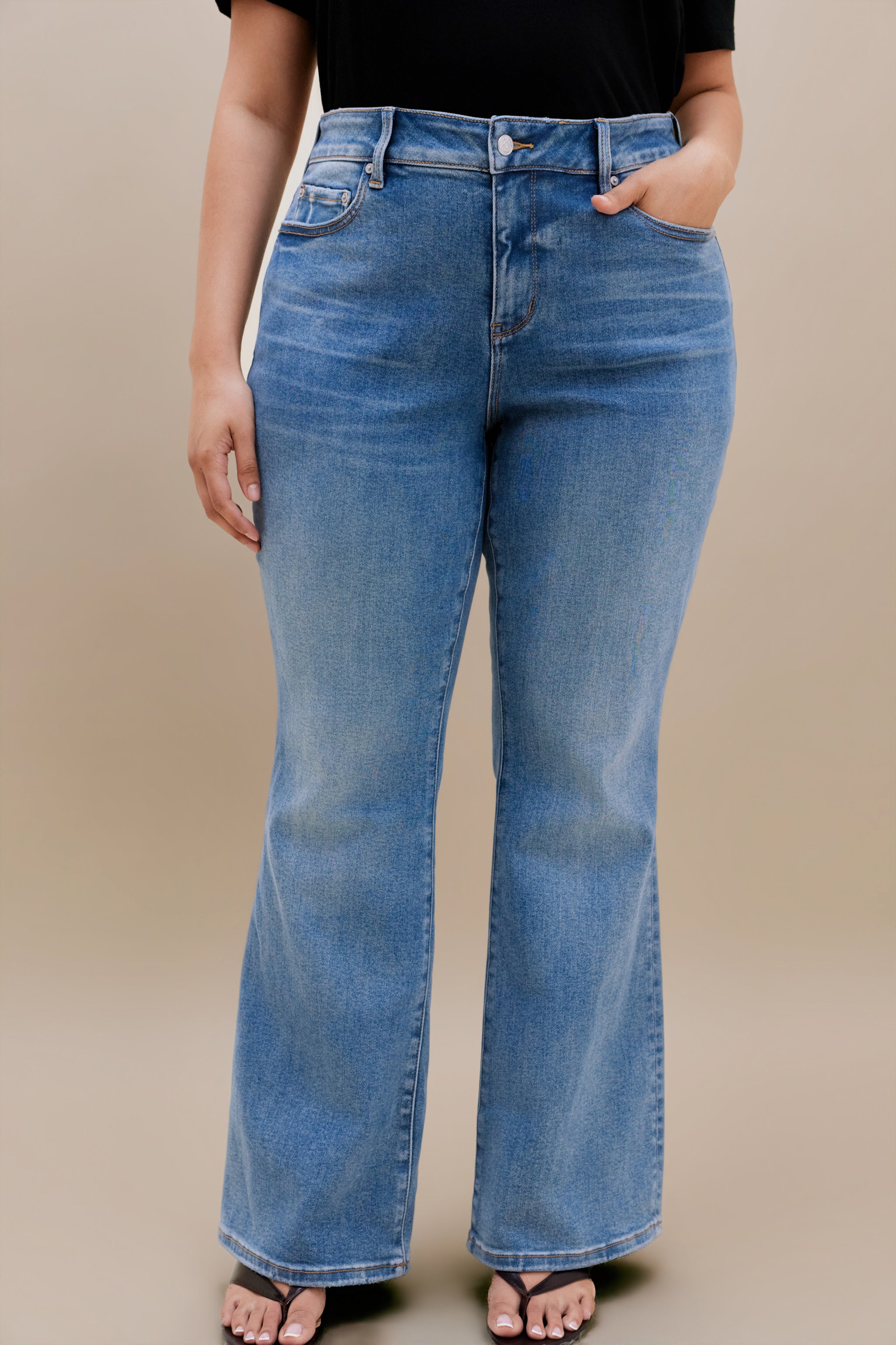 Woman wearing black t-shirt and bootcut jeans with a beige background