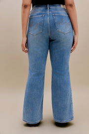 Woman wearing black t-shirt and bootcut jeans with a beige background