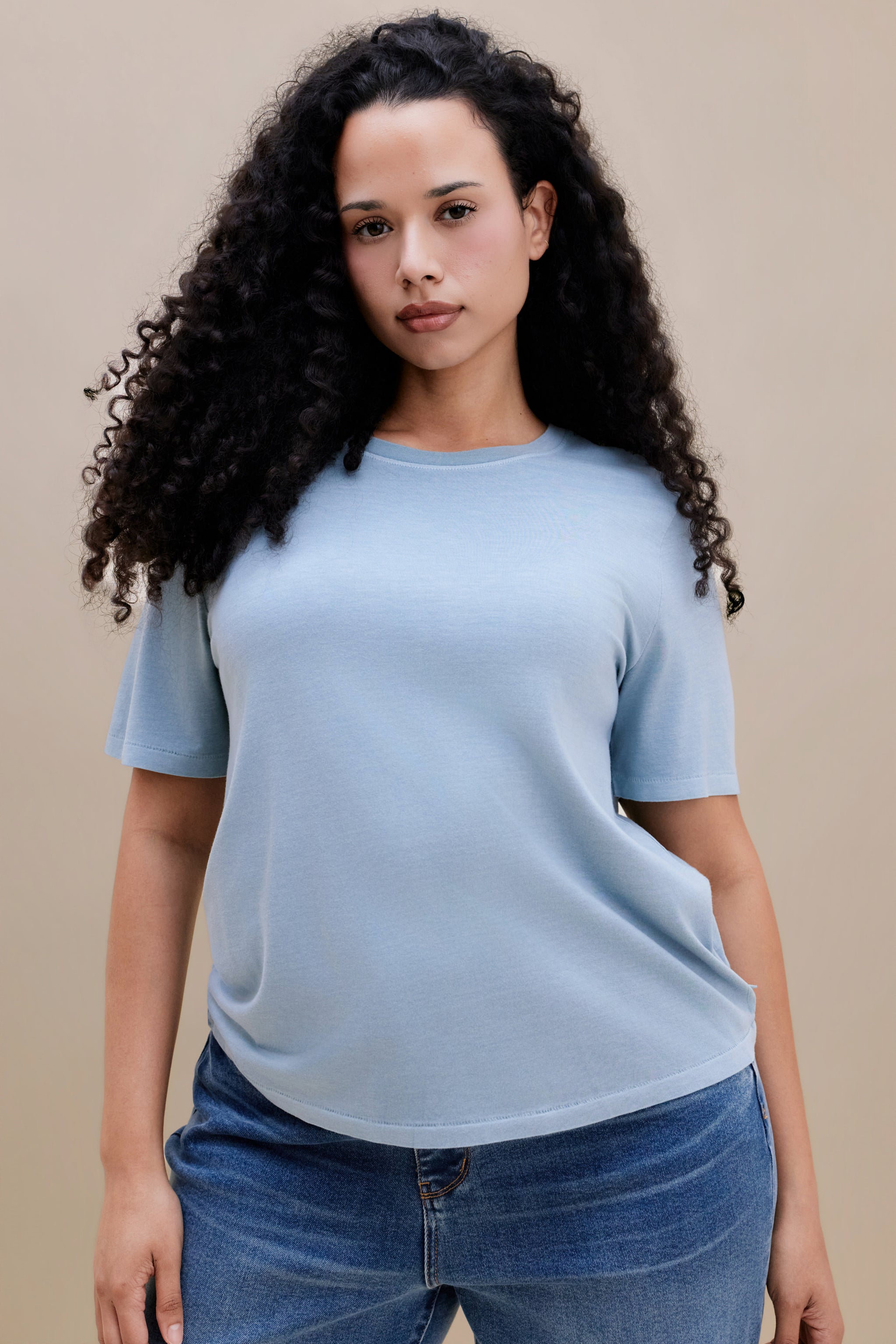 Woman wearing a light blue t-shirt and jean against a beige background | model-size: 16
