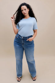 Woman wearing a light blue t-shirt and jean against a beige background 