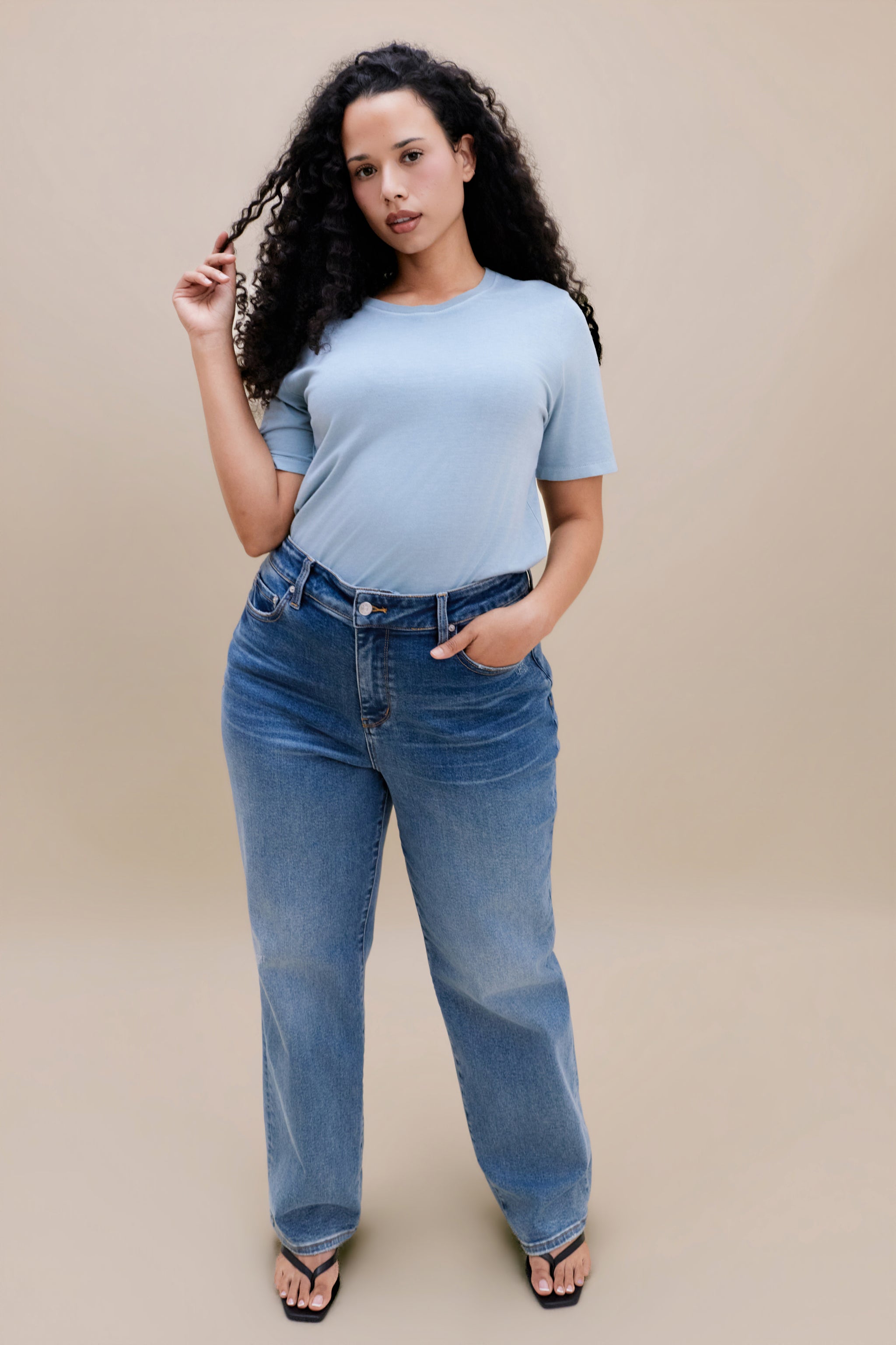 Woman wearing a light blue t-shirt and jean against a beige background 